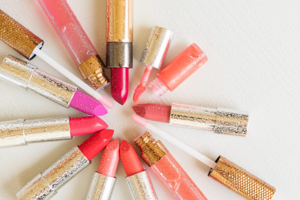 Pile of wet colourful lipsticks on wooden table, top view
