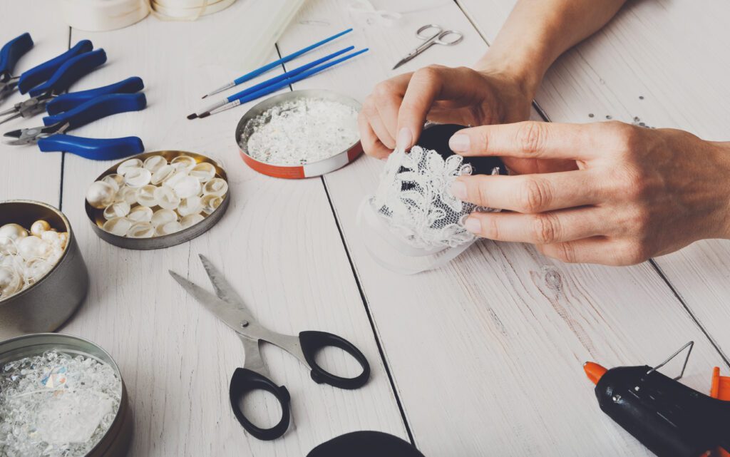 Creative diy hobby. Making handmade craft black stylish christmas balls with lace. Woman's leisure, tools for creating holiday decorations. Female hands closeup working on white wooden table