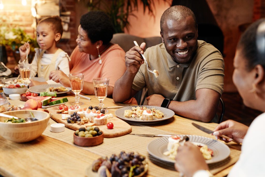 Warm toned portrait of happy African-American family enjoying dinner together outdoors with focus on smiling adult man