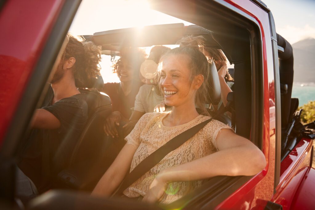 Happy millennial friends on a road trip vacation driving in an open car, close up, lens flare