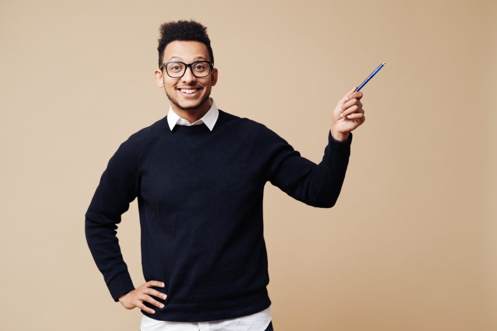 Young Professor pointing hand with pen to copy space while explaining wearing glasses on beige background. People emotions and education concept