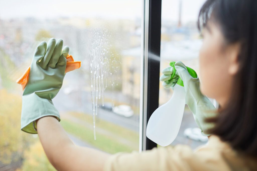 Close up of unrecognizable young woman cleaning windows with spray at home, copy space